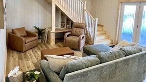 En rummelig stue med en trætrappe, sofasæt og sofabord.