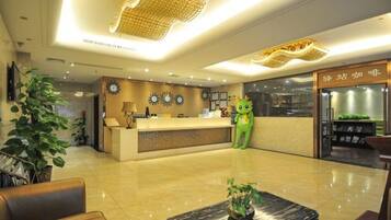 A hotel reception area with a reception desk, a green plush toy, and a plant.