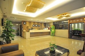 Zona de recepción de un hotel con mostrador, un peluche verde y una planta.