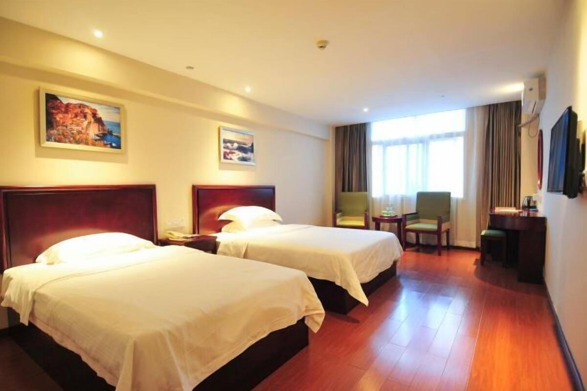 Een hotelkamer met twee bedden, een bureau, een stoel en een raam met gordijnen.