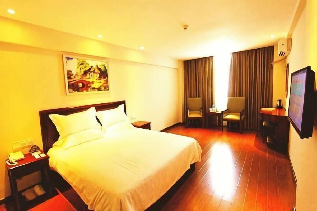 Een hotelkamer met een groot bed, een bureau, een stoel, een televisie en een schilderij aan de muur.