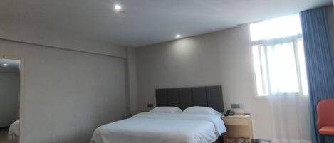 A hotel room with a bed, a bedside table, a chair, a window with curtains, and a mirror on the wall.