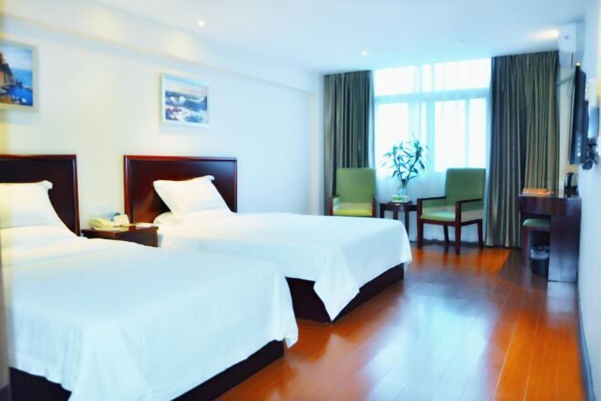 A hotel room with two beds, a small table with a plant, a chair, and a TV mounted on the wall.