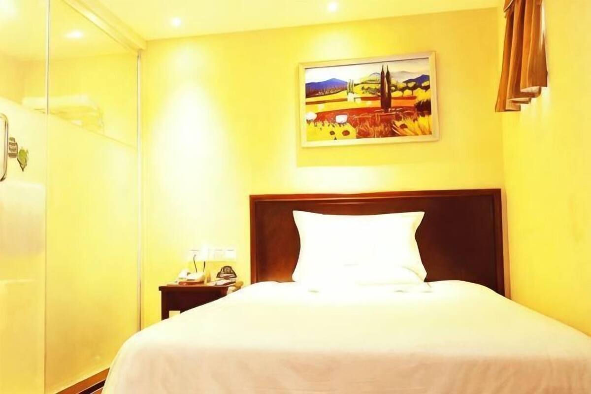 Een hotelkamer met een bed, nachtkastje, schilderij aan de muur en een douche.