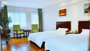 A hotel room with two beds, a desk, a chair, a plant, and a painting on the wall. - GreenTree Inn Hainan Haikou Qilou Old Street Haifu Road Express Hotel (Haikou)