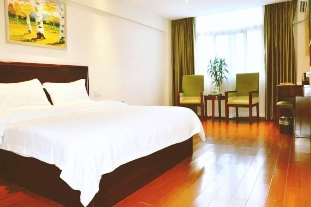 Een hotelkamer met een groot bed, twee stoelen, een klein tafeltje en een potplant.