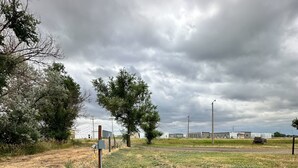 Ländliche Landschaft mit einem Feld, einigen Bäumen und einem in der Ferne liegenden Gebäudekomplex.