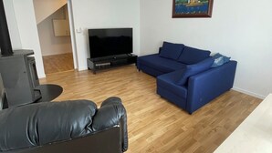 A living room with a TV, blue sofa, black leather chair, wooden flooring, and a painting on the wall. - Comfortable 2-bedroom apartment with WiFi in Lovely Plieningen! (Stuttgart)
