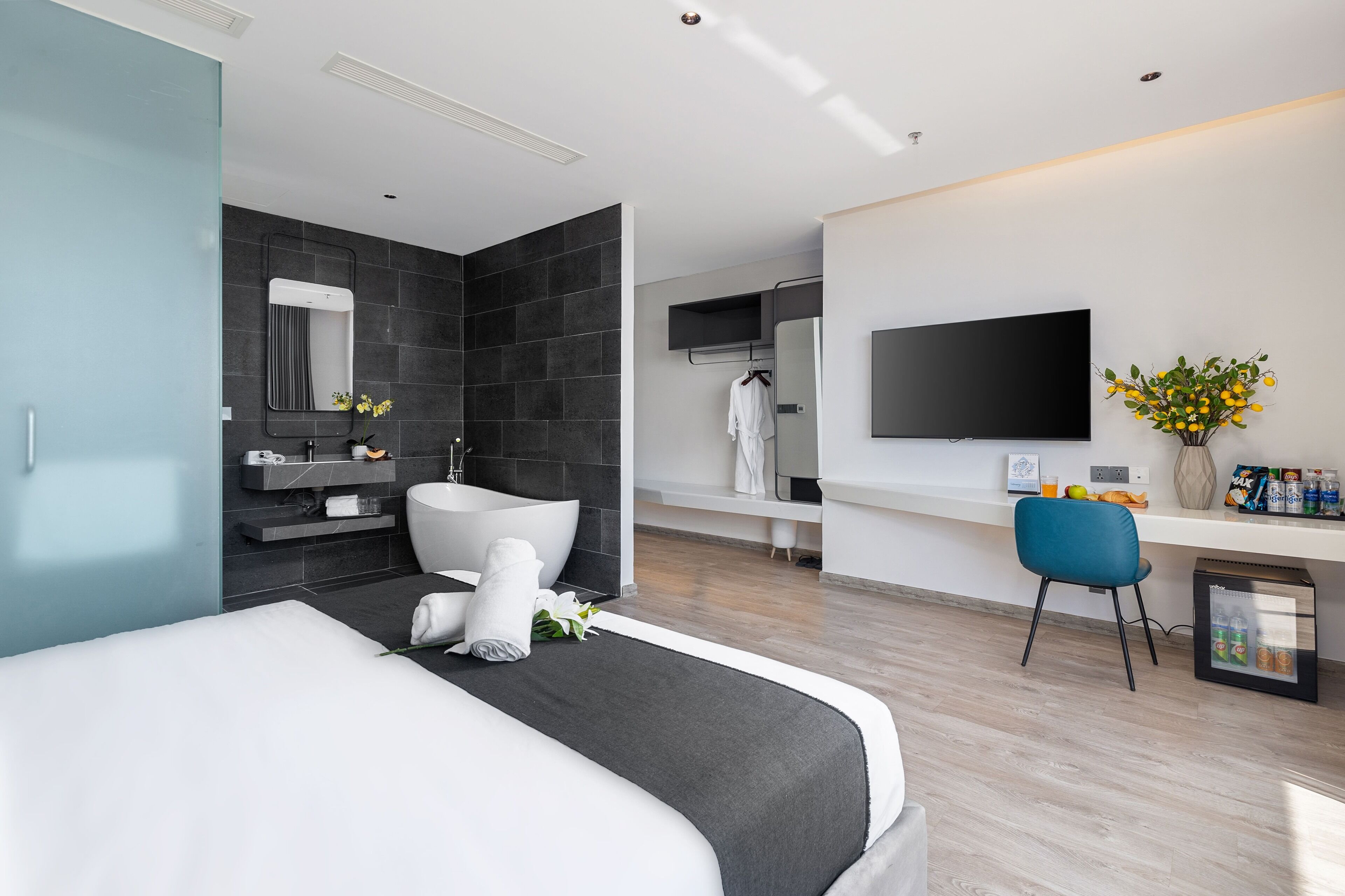 A modern hotel room with a large bed, a bathroom with a bathtub, a flat-screen TV, and a minibar.