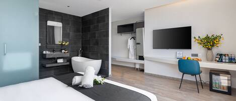 A modern hotel room with a large bed, a bathroom with a bathtub, a flat-screen TV, and a minibar.
