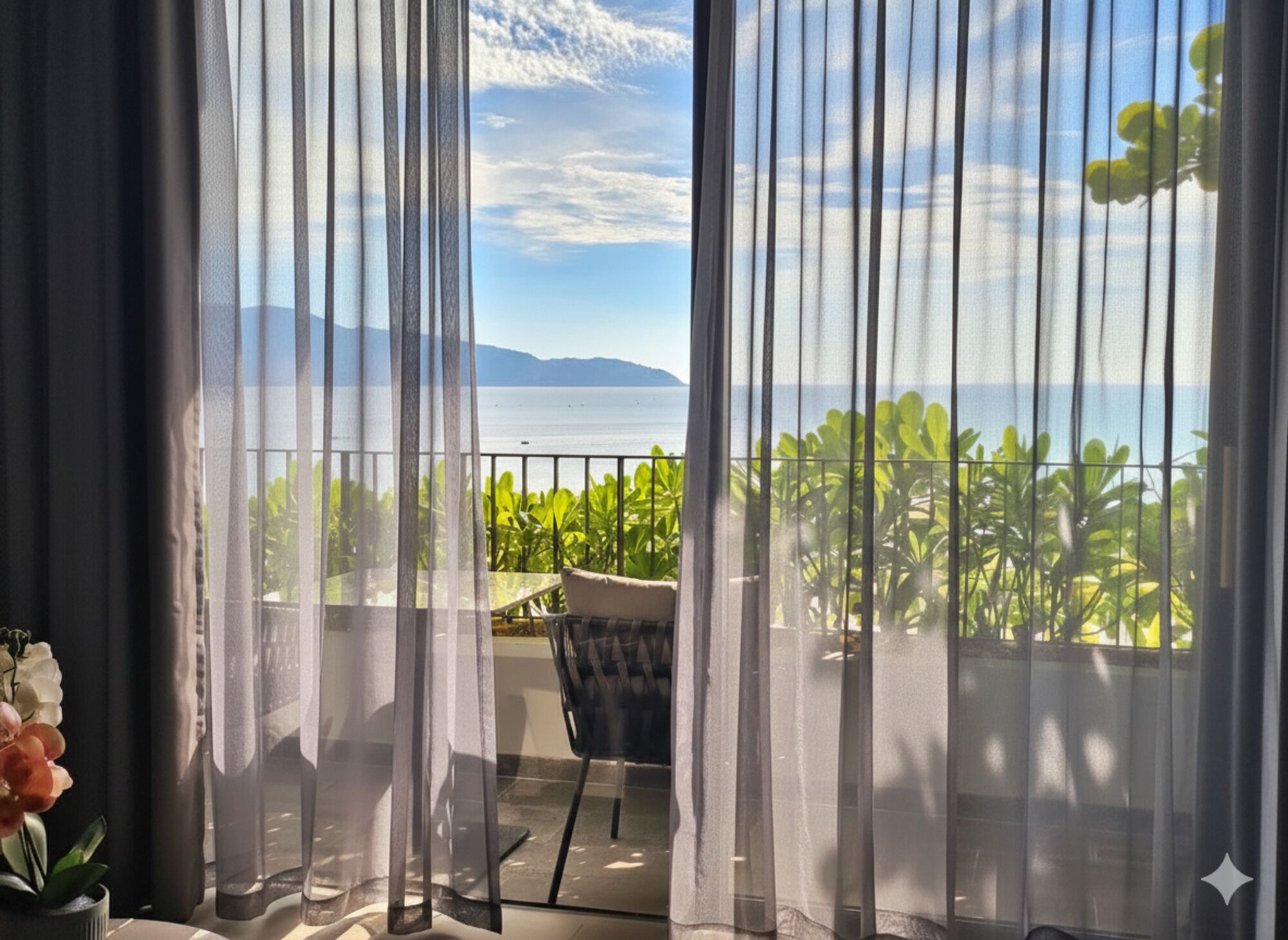 A balcony with a view of the sea and mountains, featuring a chair and potted plants.