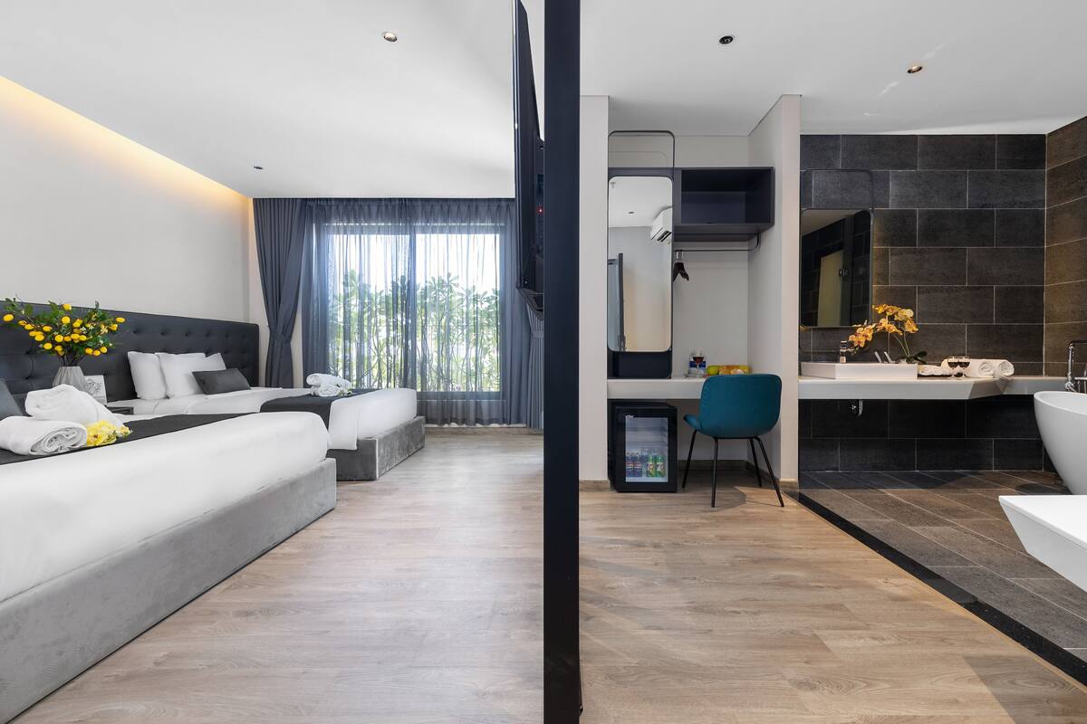 Une chambre d’hôtel moderne dotée d’un grand lit, d’un bureau, d’une salle de bain avec baignoire et offrant une vue sur la verdure environnante.