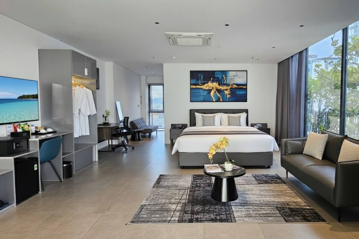 Une chambre d’hôtel moderne dotée d’un grand lit, d’un canapé, d’un bureau avec un ordinateur et d’un téléviseur offrant une vue panoramique.