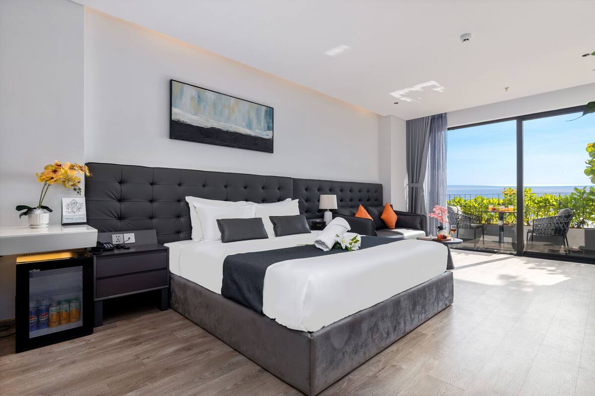 Une chambre d’hôtel moderne dotée d’un grand lit, d’une table de chevet, d’un petit réfrigérateur et offrant une vue sur l’extérieur.