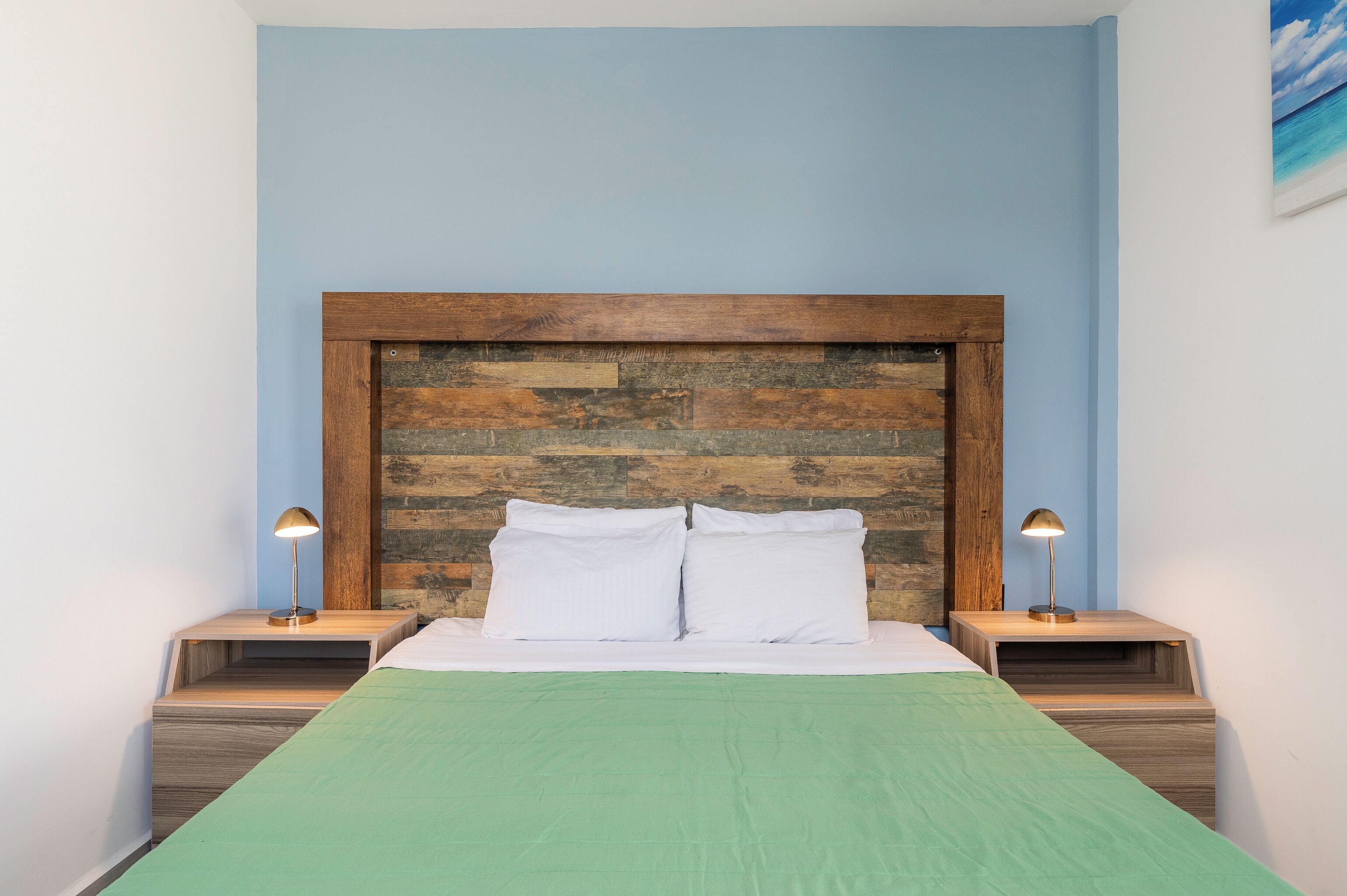 A bed with a wooden headboard, two bedside lamps, and a green bedspread.