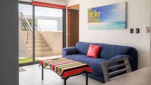 A modern living room with a blue sofa, a colorful striped table, and a painting of a beach scene. - Eden in the heights. Terrace and private pool centre and playa (Playa del Carmen)