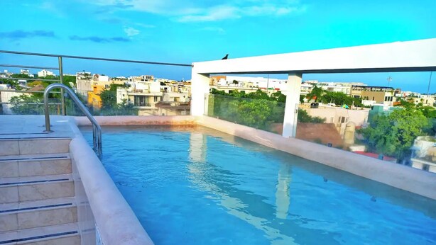 A rooftop swimming pool with steps leading into the water, surrounded by a white structure and a view of the cityscape. - Eden in the heights. Terrace and private pool centre and playa (Playa del Carmen)