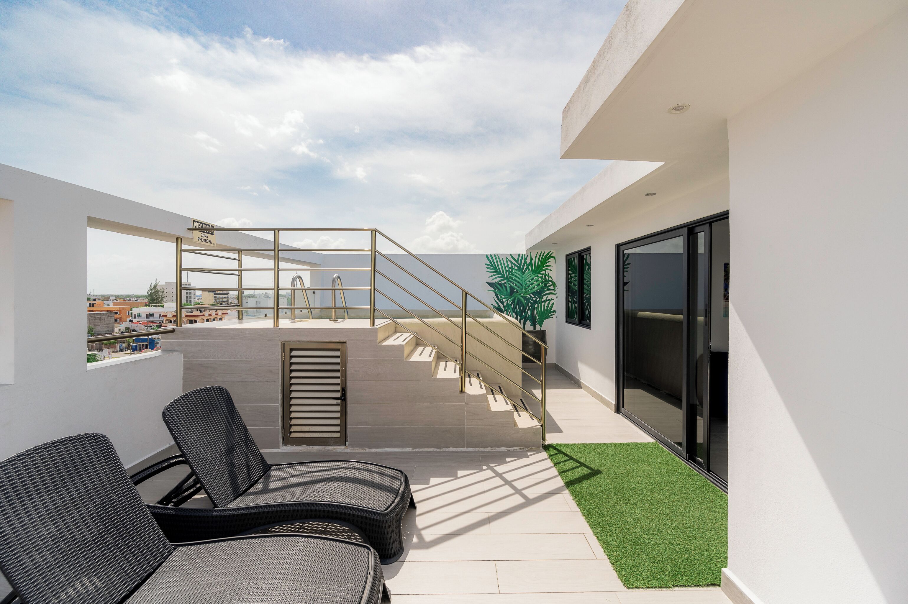 A modern rooftop terrace with a glass balustrade, outdoor seating, and a view of the cityscape.