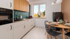 Ett modernt kök med vita skåp, en svart ugn och en matplats med ett träbord och svarta stolar.