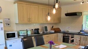 A modern kitchen with wooden cabinets, a dining table with green placemats, and a vase with purple flowers. - Spacious dog-friendly cottage in an idyllic rural setting near amazing beaches (Boncath)