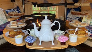 A cozy cabin interior with a central wood stove, surrounded by various food items and a white teapot on a wooden table. - Spacious dog-friendly cottage in an idyllic rural setting near amazing beaches (Boncath)