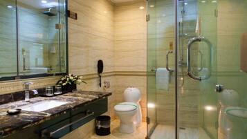 Un baño moderno con ducha envuelta en vidrio, lavamanos de mármol y un inodoro con tapa verde.