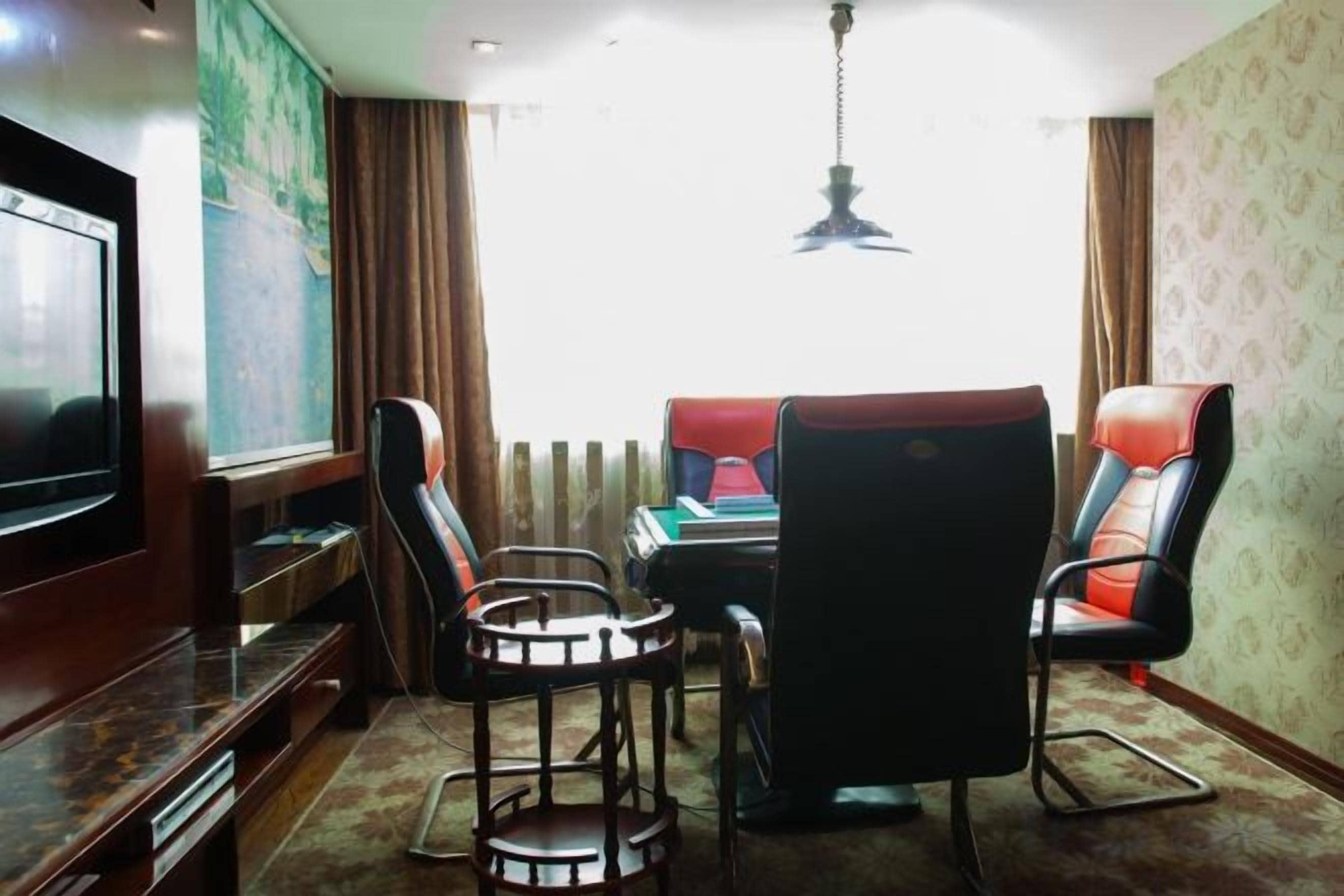 A room with a television, a dining table with chairs, a hanging light fixture, and a view through a window.