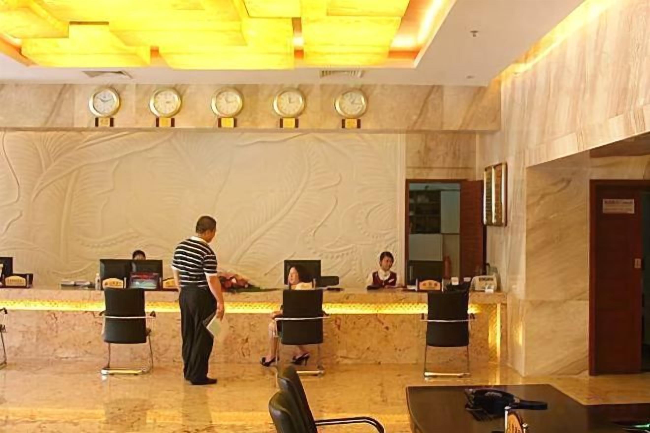 A hotel reception area with a marble counter, reception desk, and a clock above it.