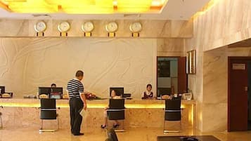 A hotel reception area with a marble counter, reception desk, and a clock above it.