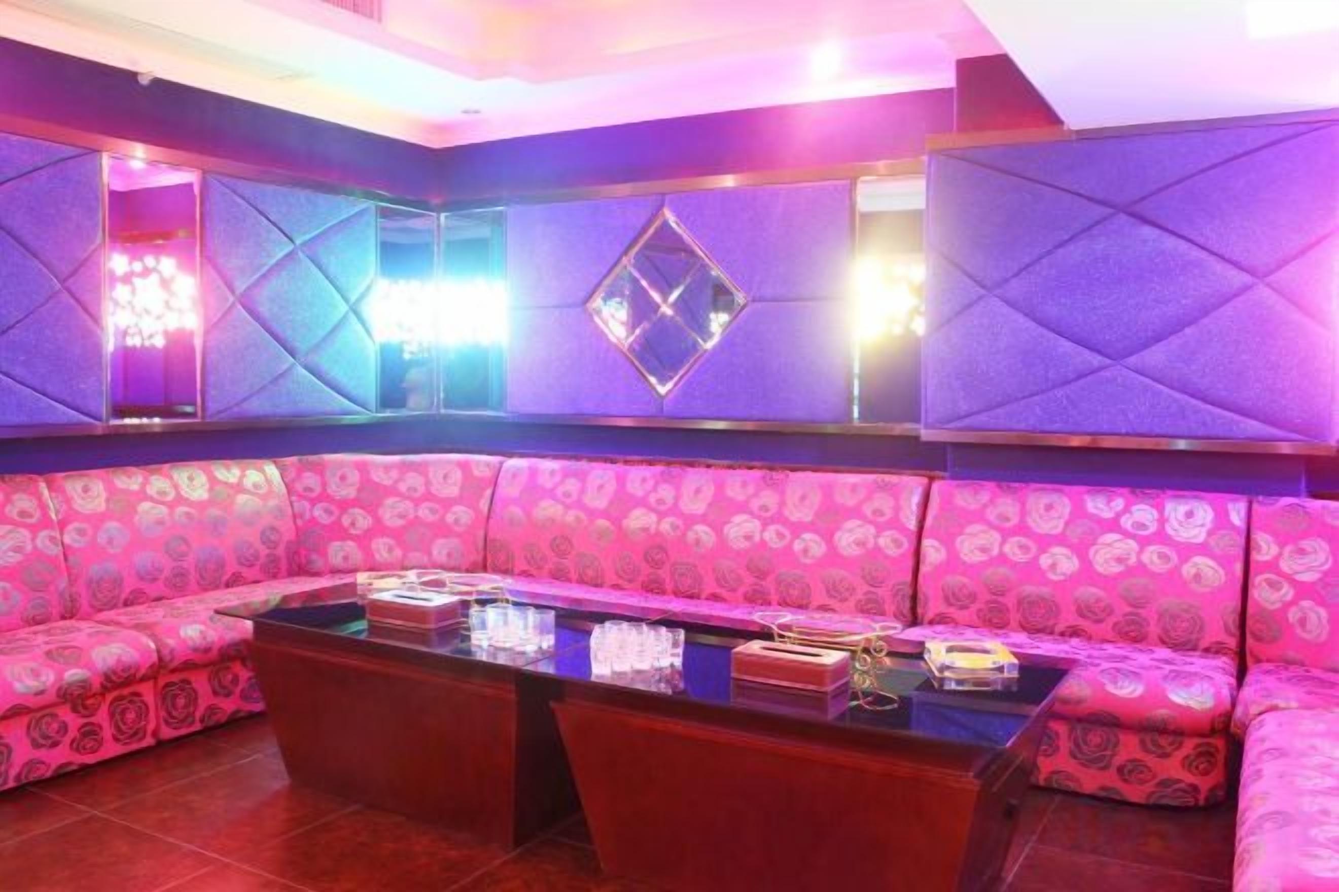 A room with a pink patterned sofa, a glass-top coffee table, and a wall with geometric patterns.