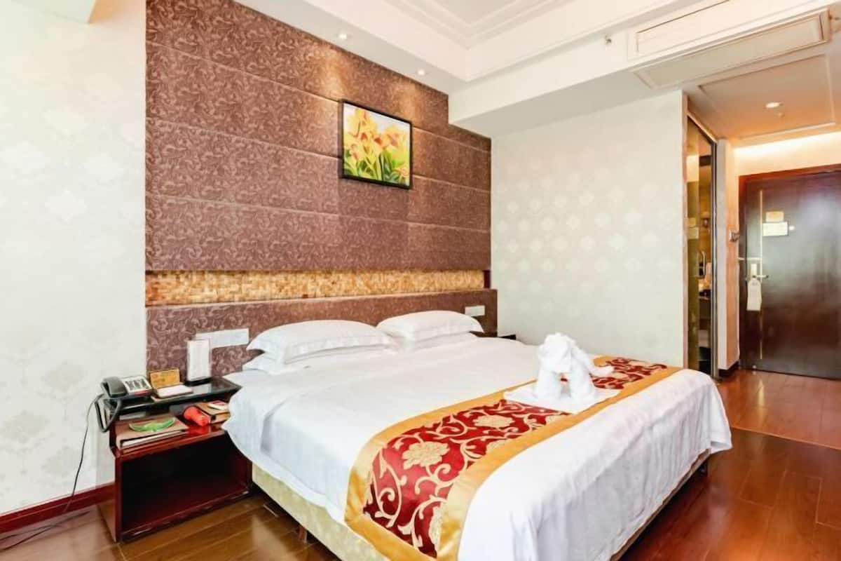 Hotellihuone, jossa on suuri sänky, yöpöytä, seinälle ripustettu taulu ja ovi oikealla puolella.