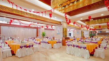 Un salón de banquetes con mesas redondas, sillas blancas y decoraciones doradas y rojas.