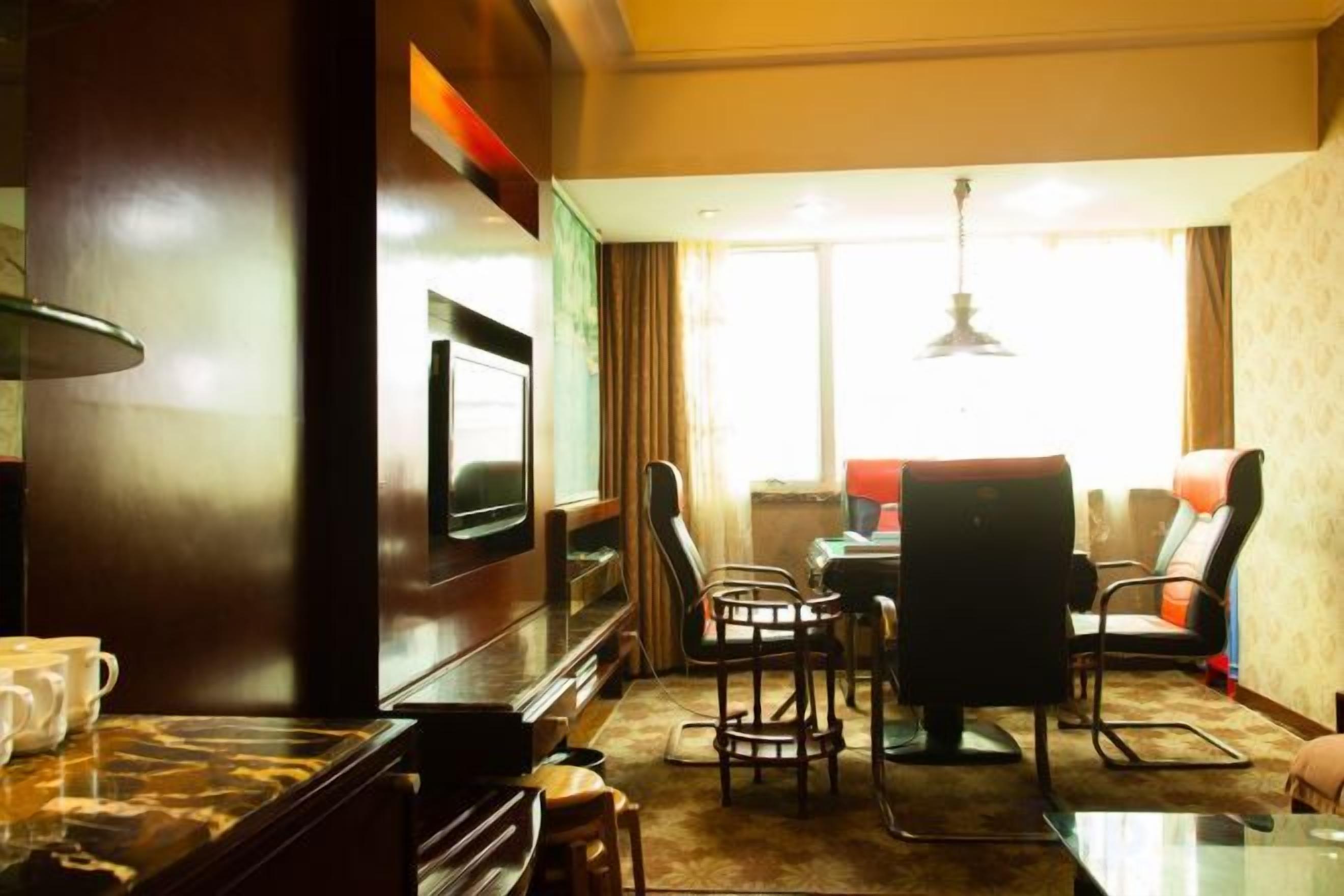 Ein Hotelzimmer mit Flachbildfernseher, Esstisch mit Stühlen, einer Sitzecke und einem großen Fenster mit Vorhängen.