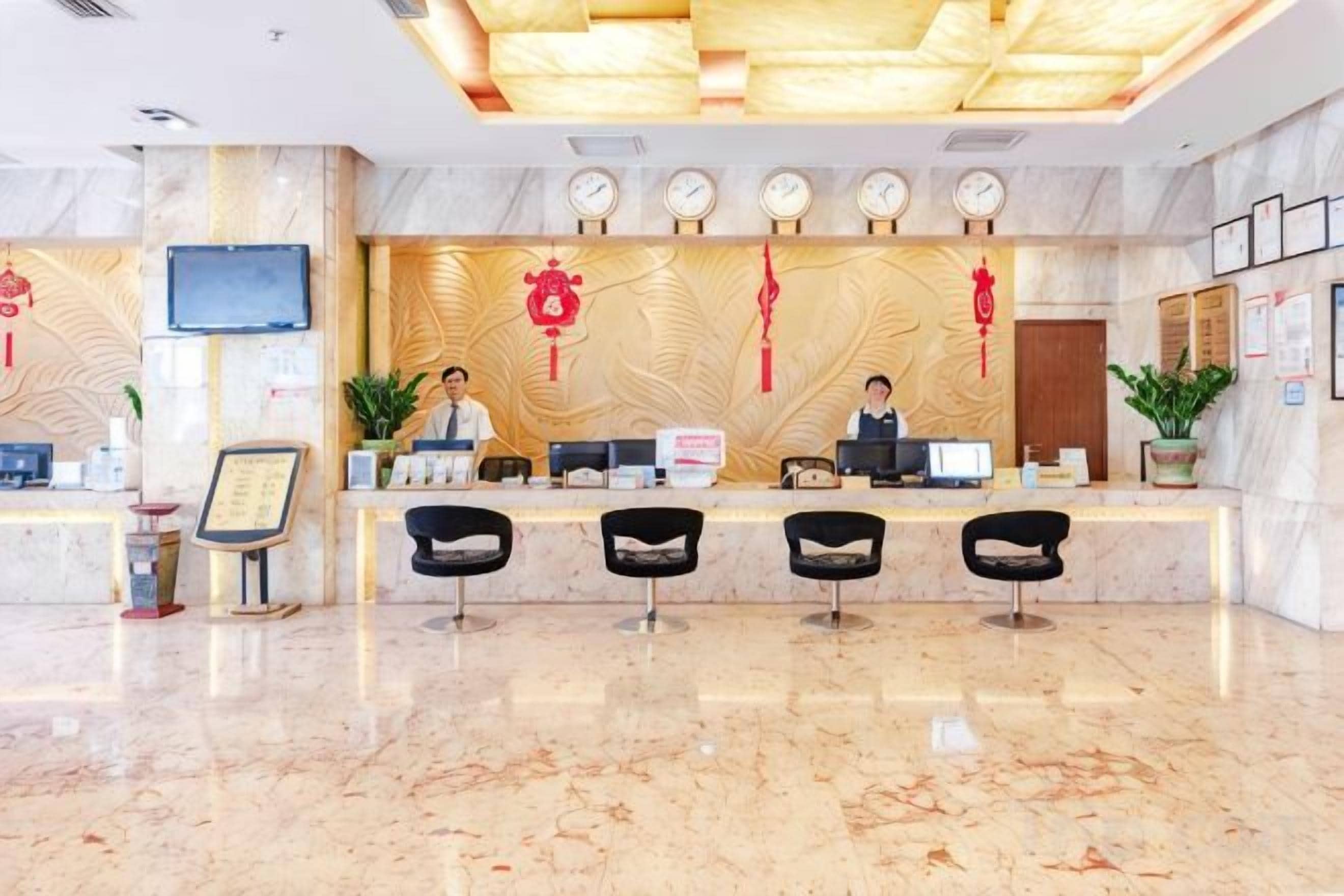A hotel reception area with a marble floor, a reception desk, and three black chairs.