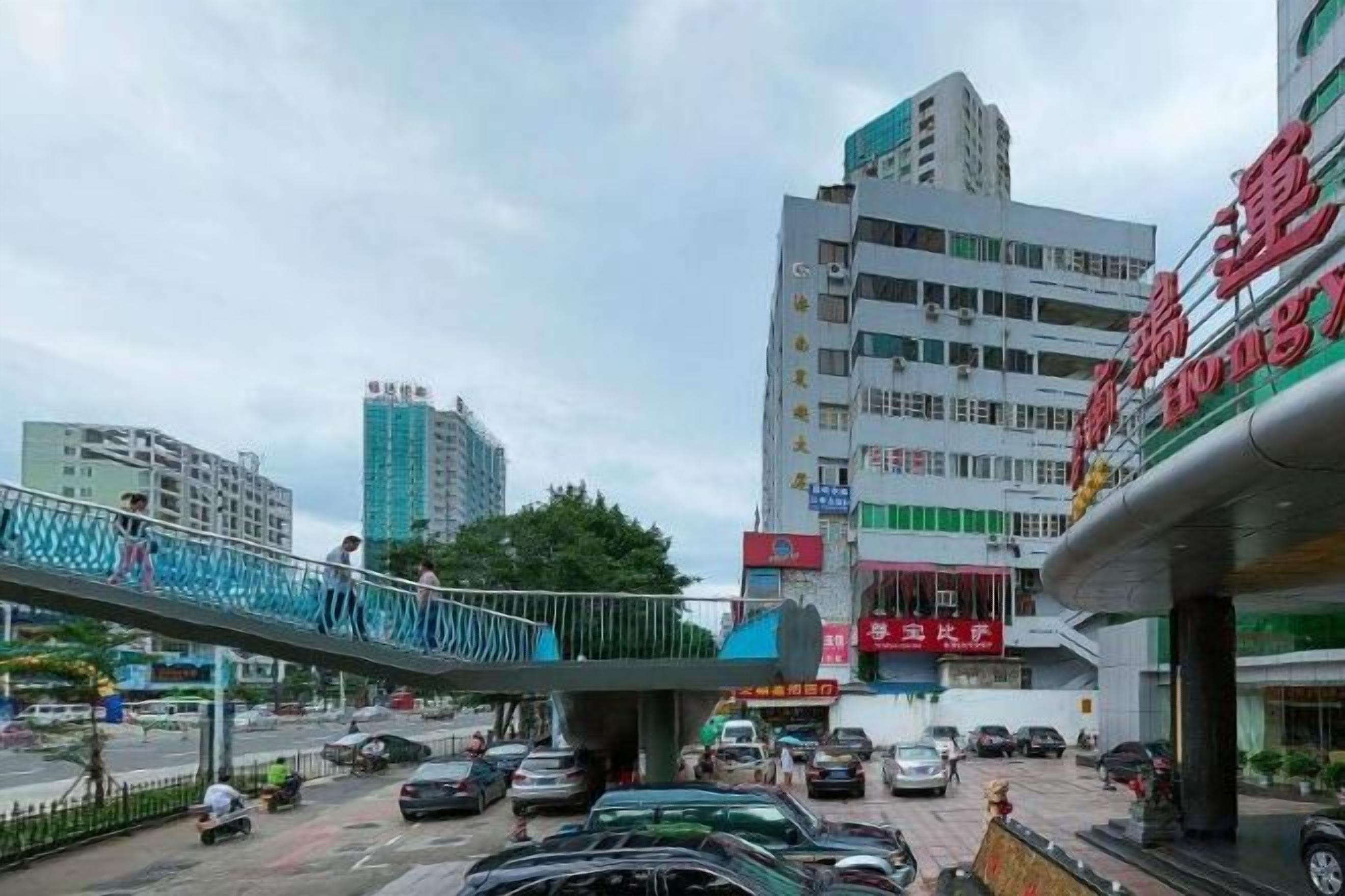 A busy urban street with a pedestrian overpass, a multi-story building with signage, and parked cars.