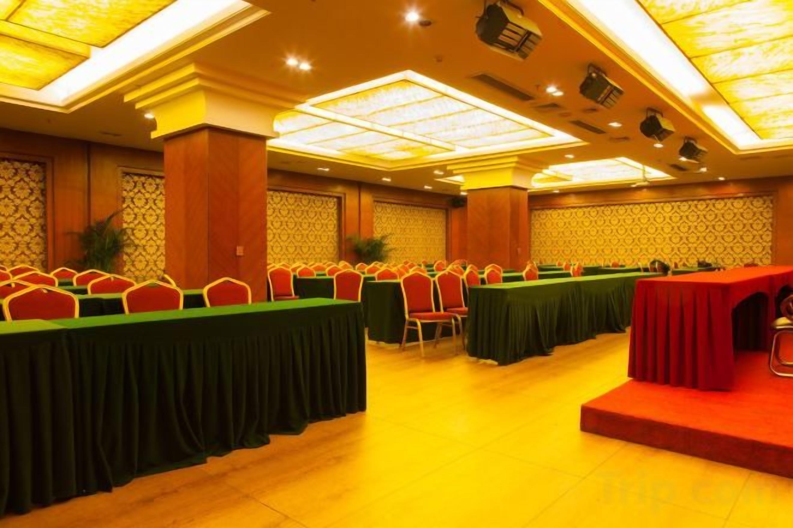 A conference room with multiple tables and chairs, a stage, and a patterned wall.