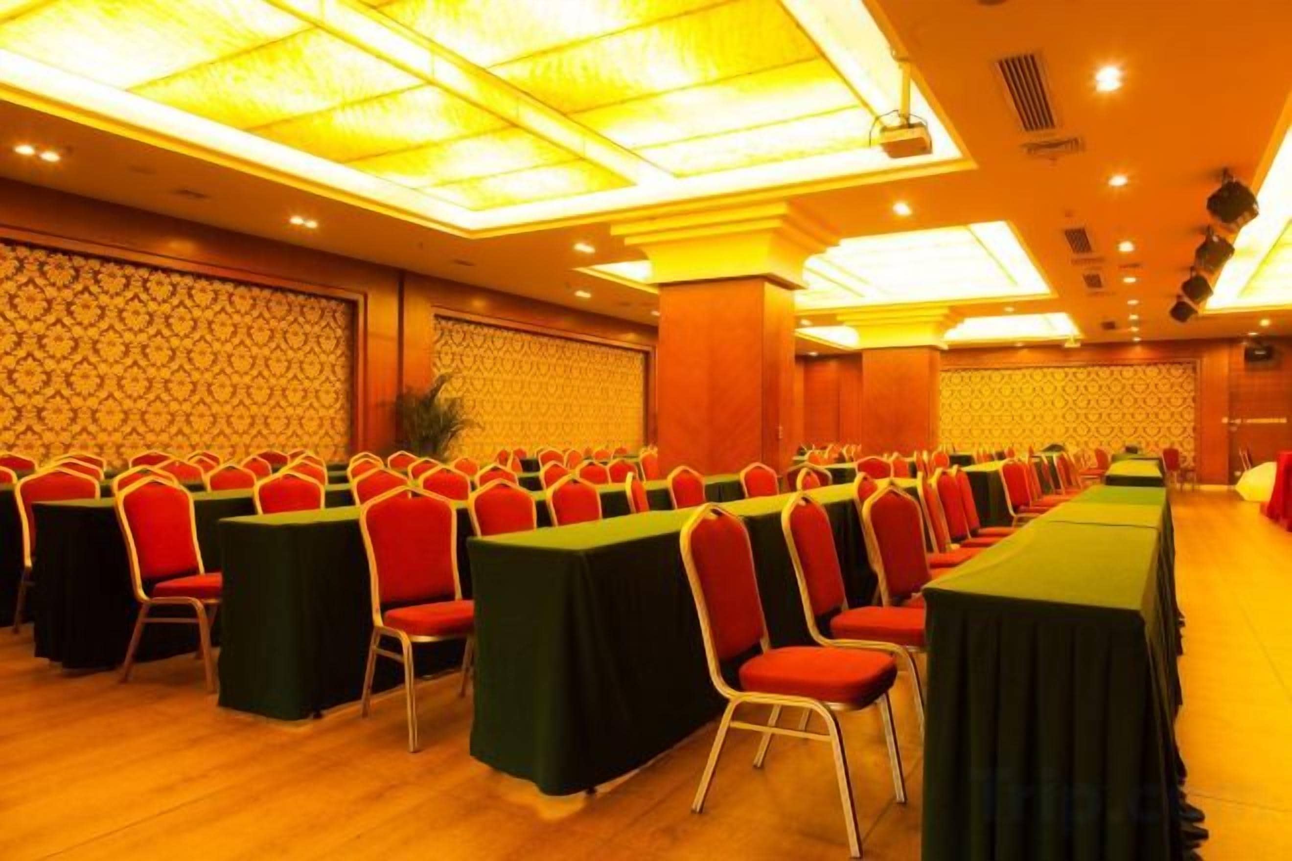 A conference room with rows of tables and chairs, a patterned wall, and a ceiling with recessed lighting.