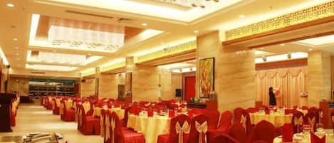 A banquet hall with rows of tables and chairs, a stage, and a large chandelier.