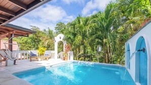 Une piscine agrémentée d’une arche blanche, entourée d’une végétation luxuriante et de palmiers.