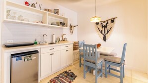 Een kleine keuken met witte kastjes, een spoelbak en een eetgedeelte met blauwe stoelen.