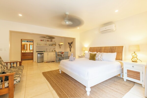 A bedroom with a large bed, bedside tables, a nightstand, a ceiling fan, and an air conditioning unit.
