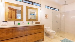 Een moderne badkamer met een houten wastafelmeubel, twee spiegels, een toilet en een douchecabine met glazen wanden.