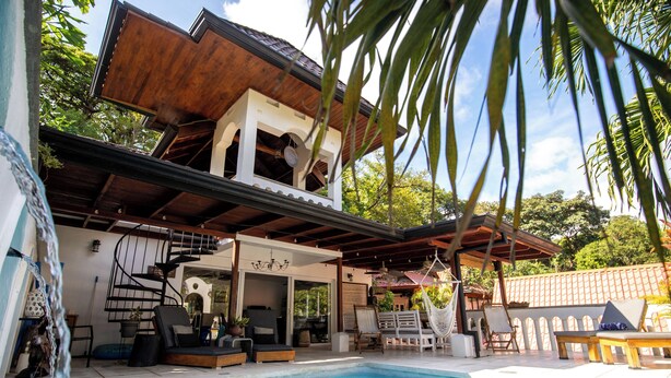 Zona de piscina con terraza de madera, sillas de descanso y una escalera espiral que conduce a un nivel superior.