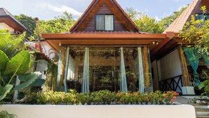 A wooden house with a triangular roof, a covered porch, and a garden with various plants and flowers.
