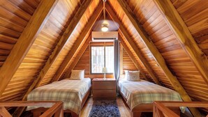 A cozy attic bedroom with wooden beams, two beds, a small table, and a window.