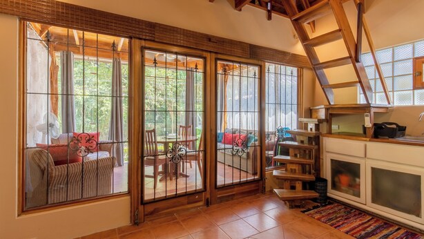A spacious room with a large sliding glass door leading to an outdoor patio area. There is a wooden staircase with a view of the patio, and a kitchen area with cabinets and a sink.