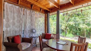 A wooden ceiling, a dining table with chairs, a sofa with cushions, and a fan.