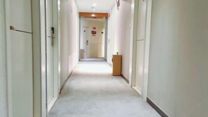 Un pasillo estrecho con alfombra, paredes blancas y una puerta de madera al final.