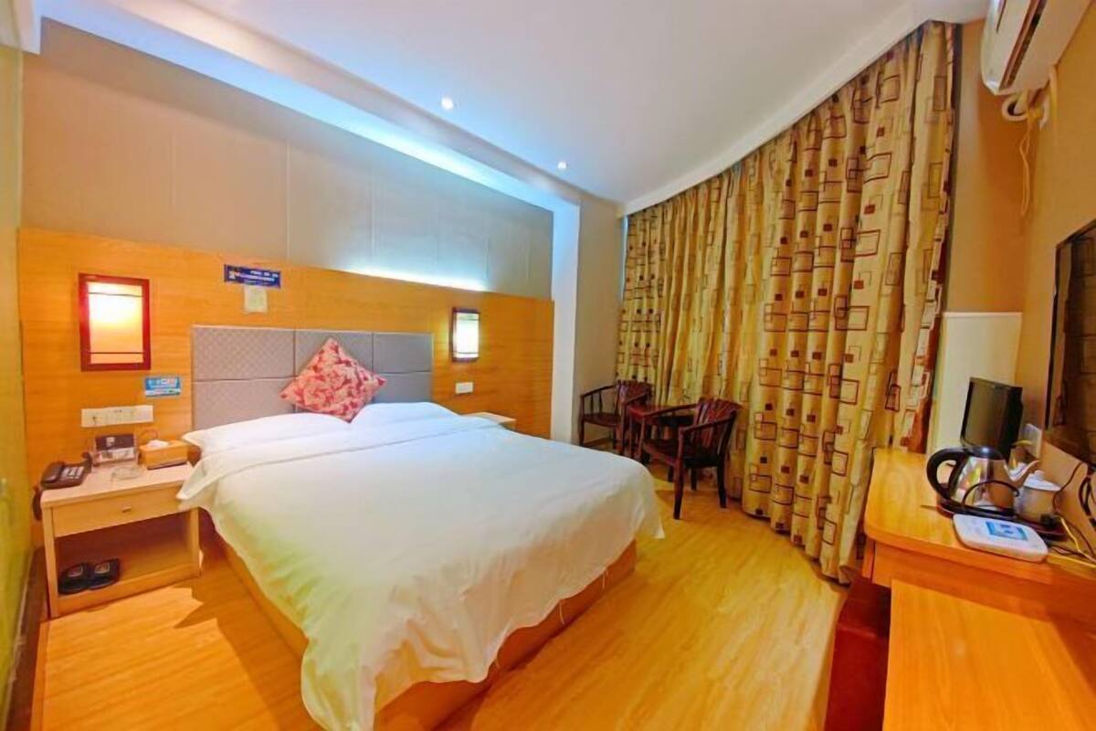 Una habitación de hotel con cama, mesita de noche, silla, escritorio y cortinas.