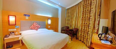 A hotel room with a bed, bedside table, chair, desk, and curtains.